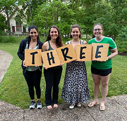 Four women holding the letters that spell three