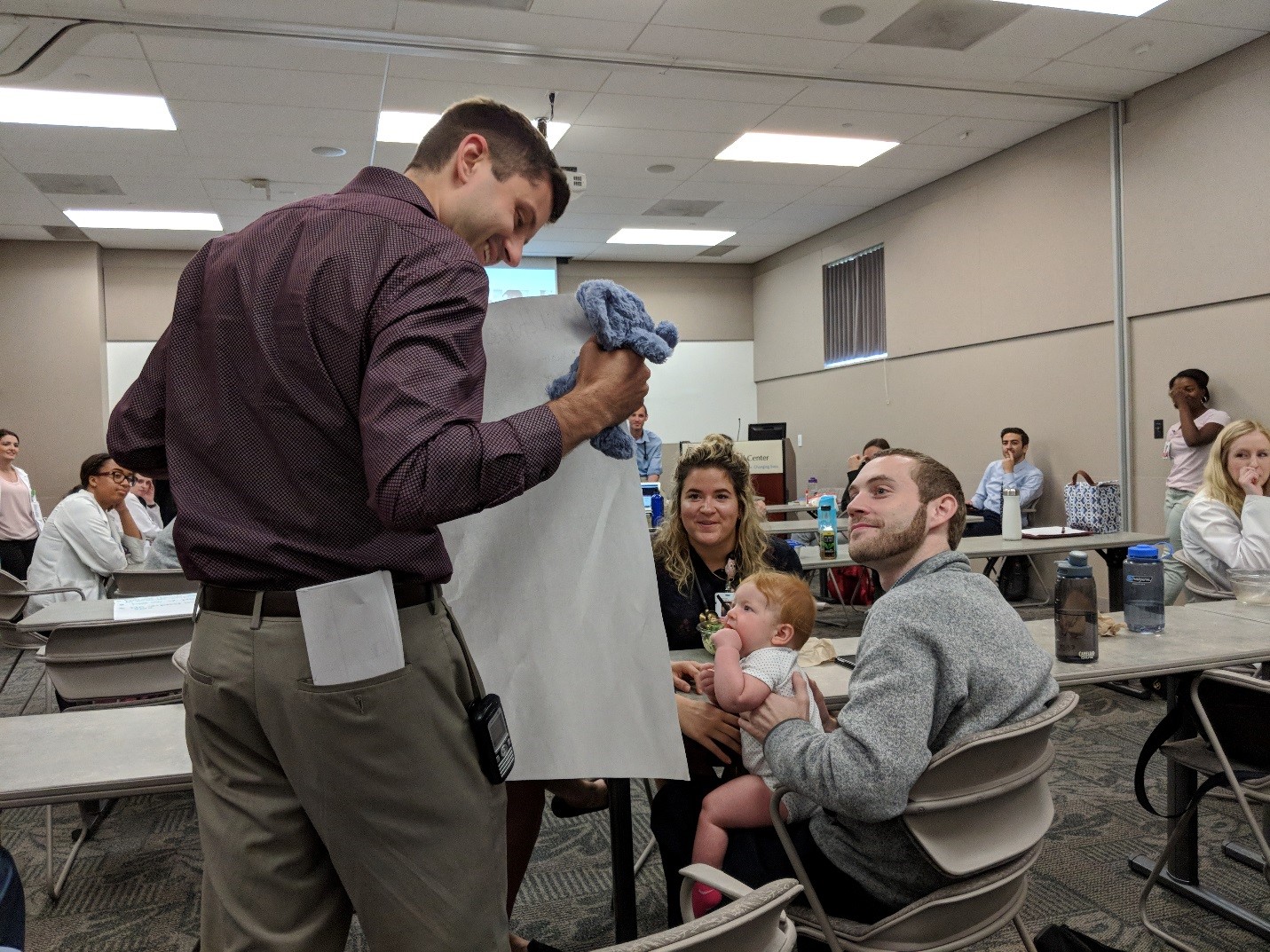 A doctor is speaking to a mother and a father with their baby. Other doctors in the room look on.