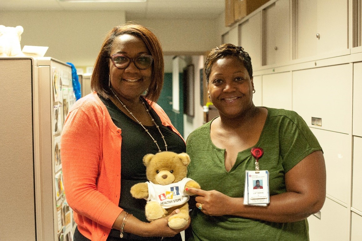 two women hold a stuffed bear toy