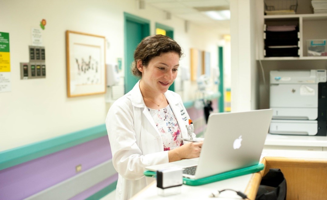 A doctor looks at a laptop computer in a hospital hallway